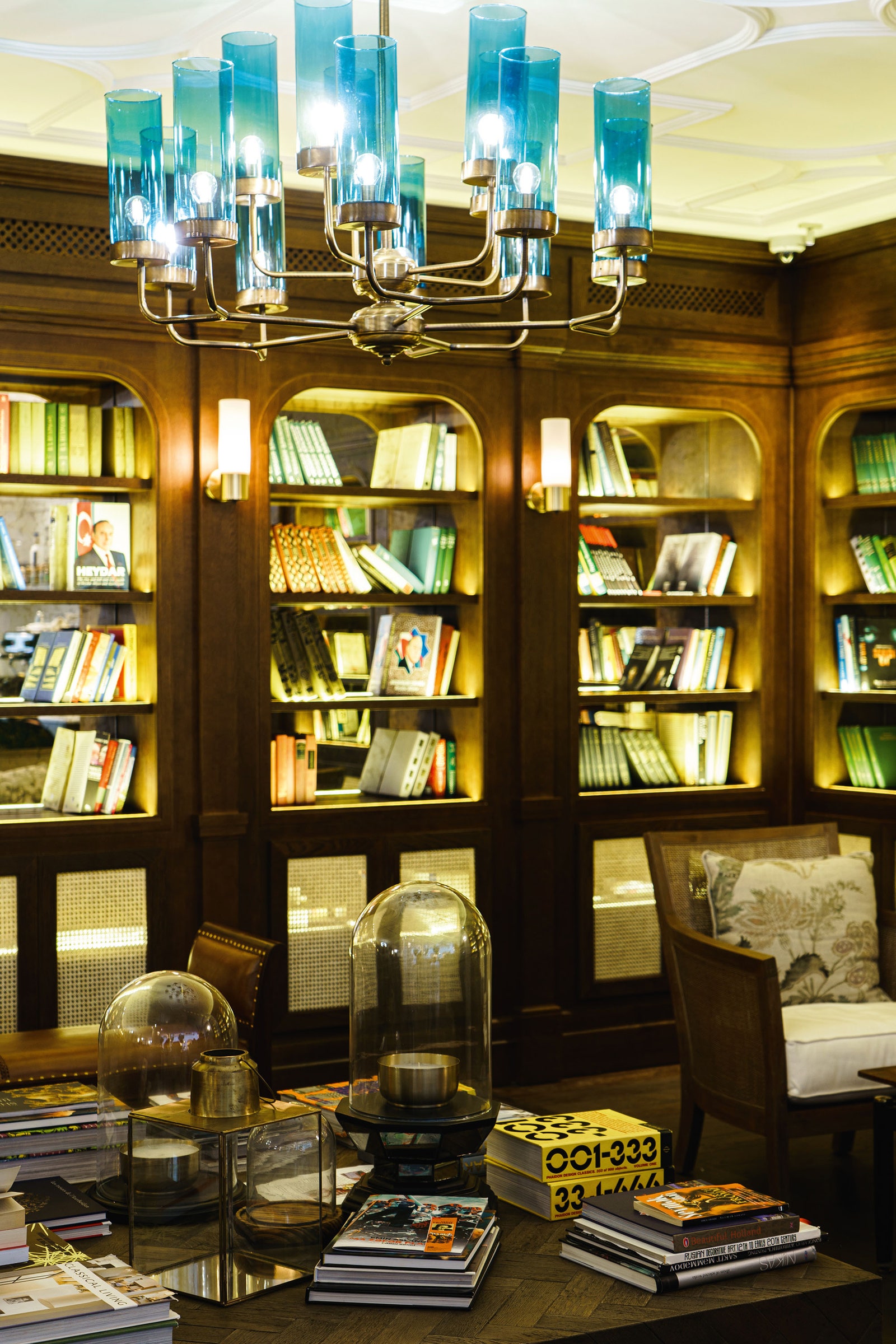青いガラス製品のランプに照らされた部屋に並ぶ本でいっぱいの木の棚